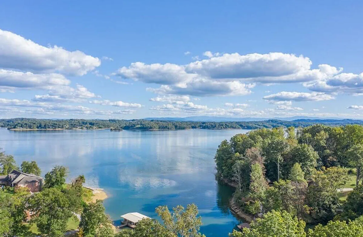 A wide, tranquil view of Cherokee Lake, framed by gentle clouds, a forested shoreline, and distant hills. The image captures the essence of lakeside recreation—boating, fishing, and peaceful sunset moments—central to the getaway experience described in the section.