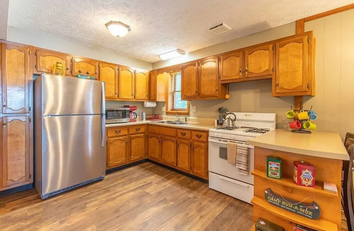 This interior image centers on a modern kitchen featuring a stainless steel refrigerator, wooden cabinets, a kitchen sink, and a stove. The scene feels warm and welcoming, set up for cooking and hosting family gatherings. Ample counter space and visible appliances convey a sense of readiness for culinary activity.