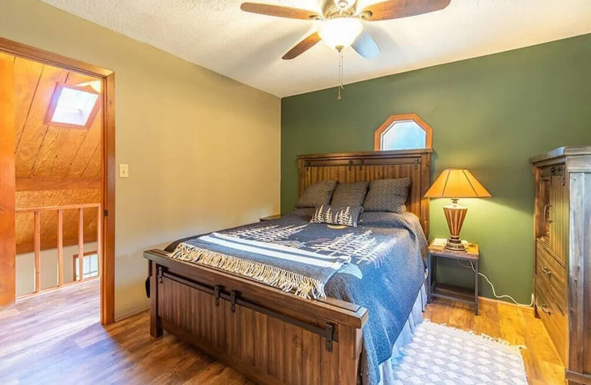 A tranquil bedroom scene showcasing a bed, wooden furniture, a lamp, and a window letting in soft natural light. The peaceful mood emphasizes rest, relaxation, and being surrounded by nature. The presence of the window suggests proximity to the outdoors, reinforcing the connection to the natural setting.