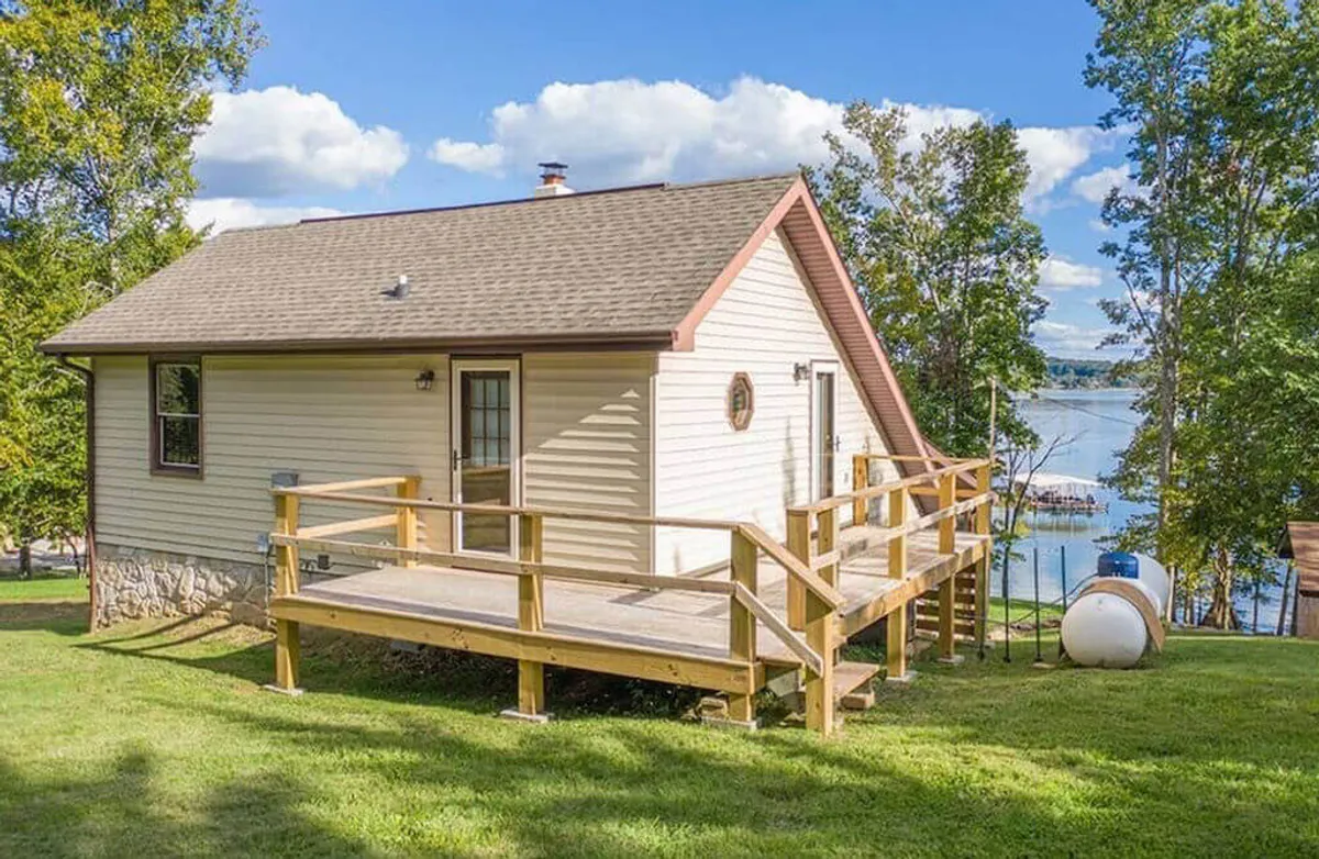 A welcoming wooden deck attached to the house, furnished for relaxing or dining, with a clear view of Cherokee Lake in the background. The area is set up for both morning coffee and evening grilling, with the lake's edge visible and hints of seasonal foliage surrounding the space.