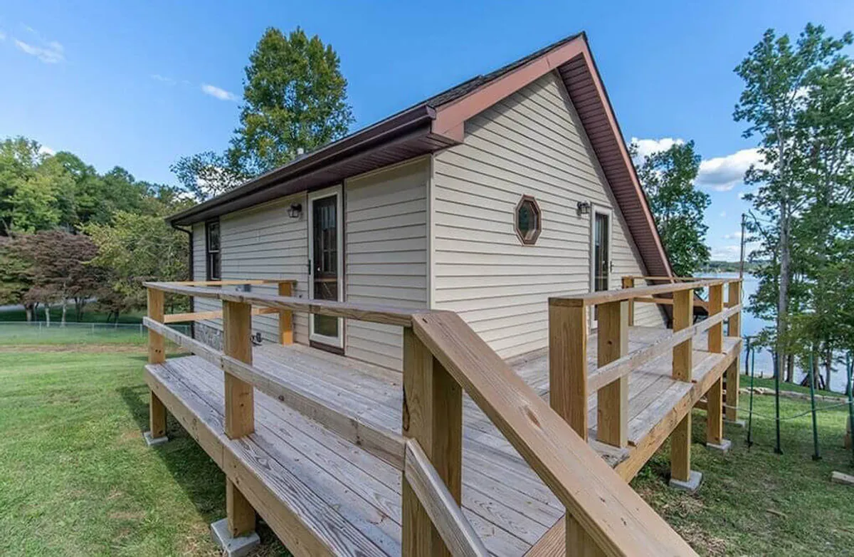 This image showcases the cottage's inviting wooden deck, surrounded by lush trees and with a glimpse of the house exterior. The setting is perfect for small group gatherings, outdoor meals, and unwinding in nature, echoing the section's emphasis on togetherness and relaxation.
