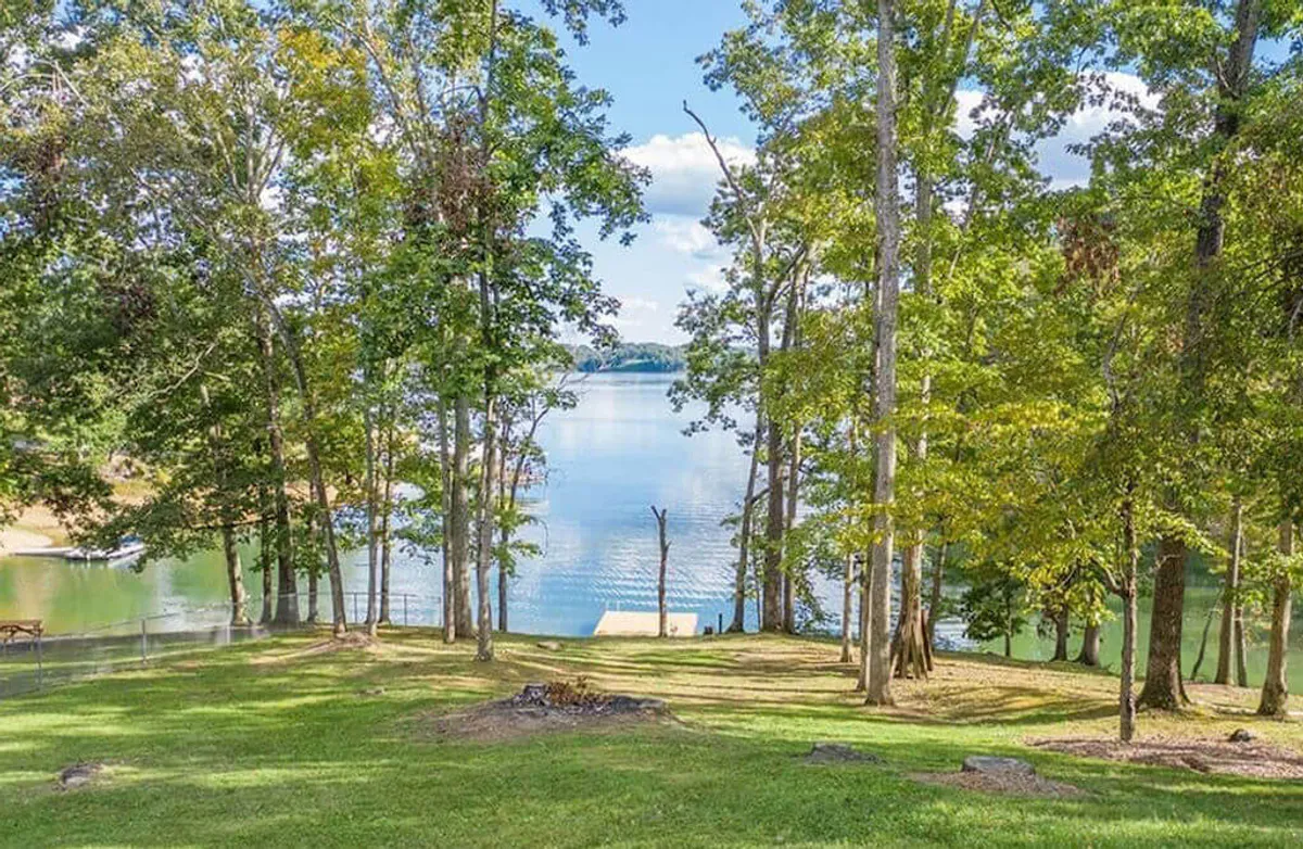 A broad lakefront scene featuring a dock extending into the tranquil waters, surrounded by trees and grassy areas. This view captures the changing beauty of the lake across seasons and hints at the recreational opportunities available just steps from the porch.